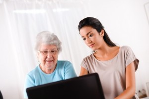 cheerful young woman teaching computer and internet to elderly person